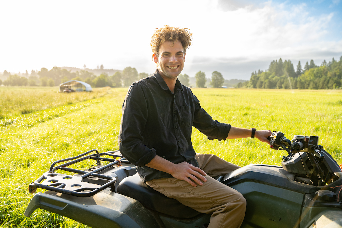 Young farmer sitting on an ATV in a bright green field at sunset.