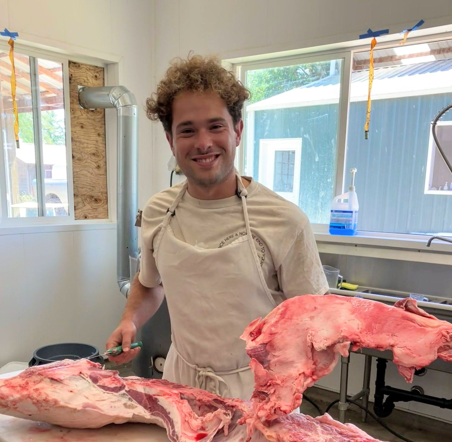 Farm worker in a butcher room holding a large cut of meat.