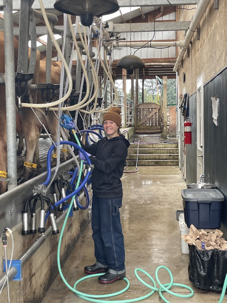 Farmer standing in a dairy parlor beside milking equipment and cows.
