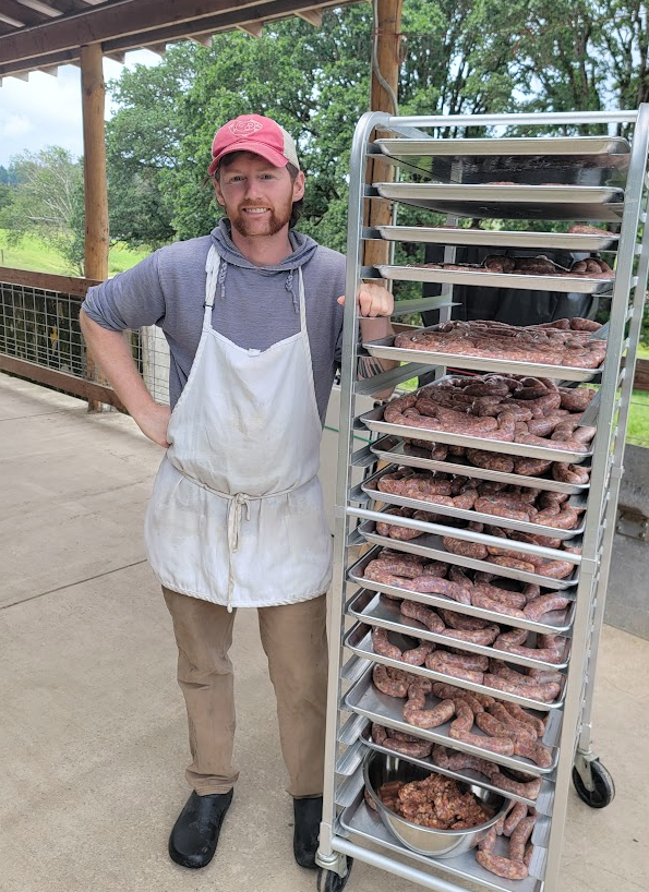 Farm worker standing beside a rack full of sausages in a processing space.